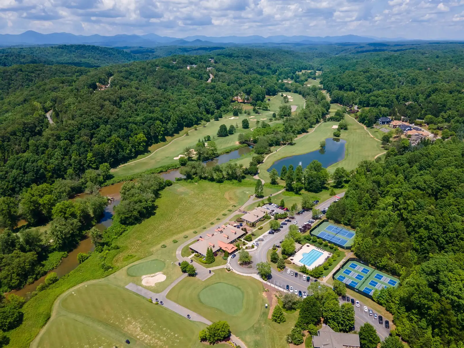 Wide aerial drone view of the Achasta community core in Dahlonega Georgia &mdash; clubhouse, tennis and pickleball courts, swimming pool, golf course, Chestatee River, and Blue Ridge foothills