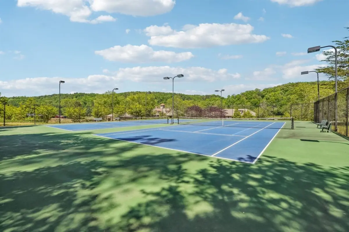 Two hard tennis courts at Achasta with light poles, with the clubhouse and tree-covered hill in the background