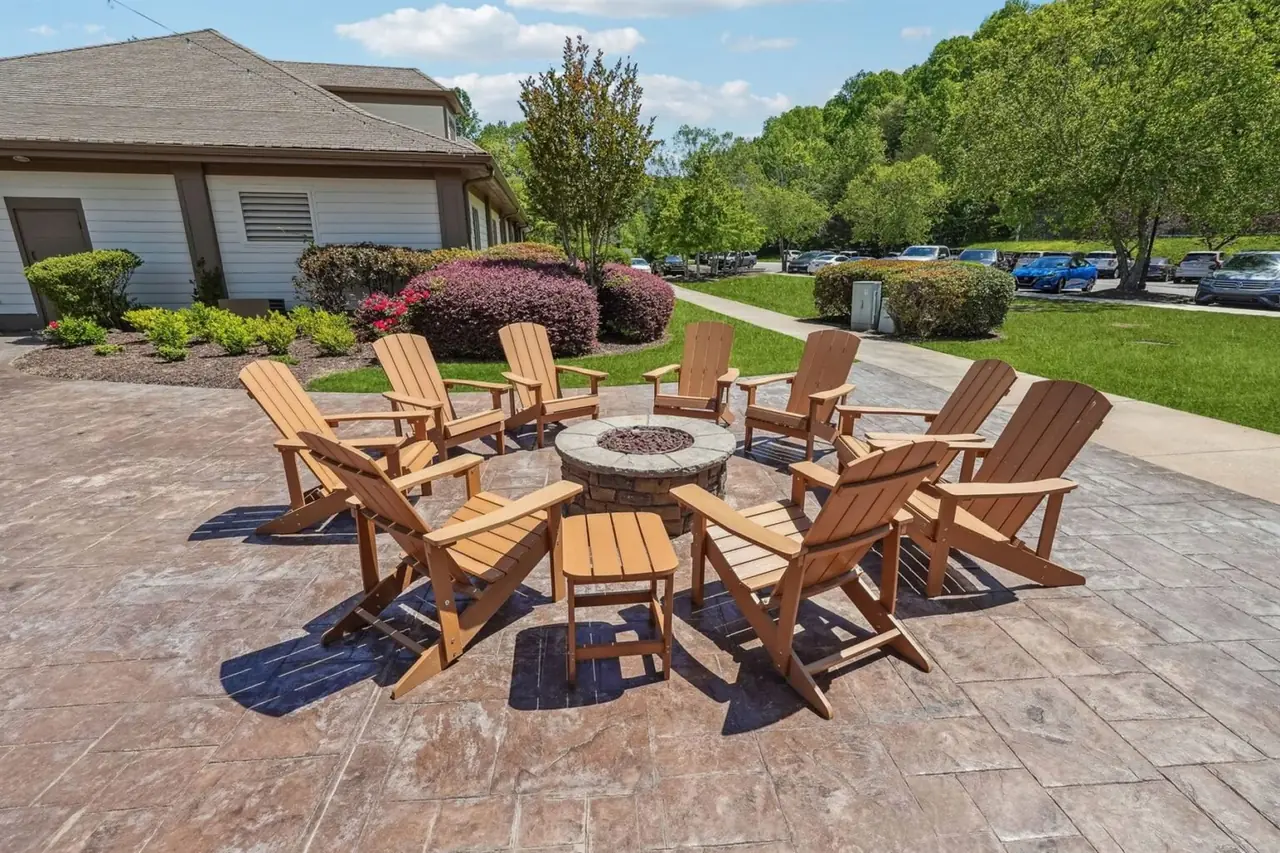 Outdoor firepit lounge at the Achasta clubhouse &mdash; eight cedar Adirondack chairs arranged around a stone gas firepit on a stamped concrete patio