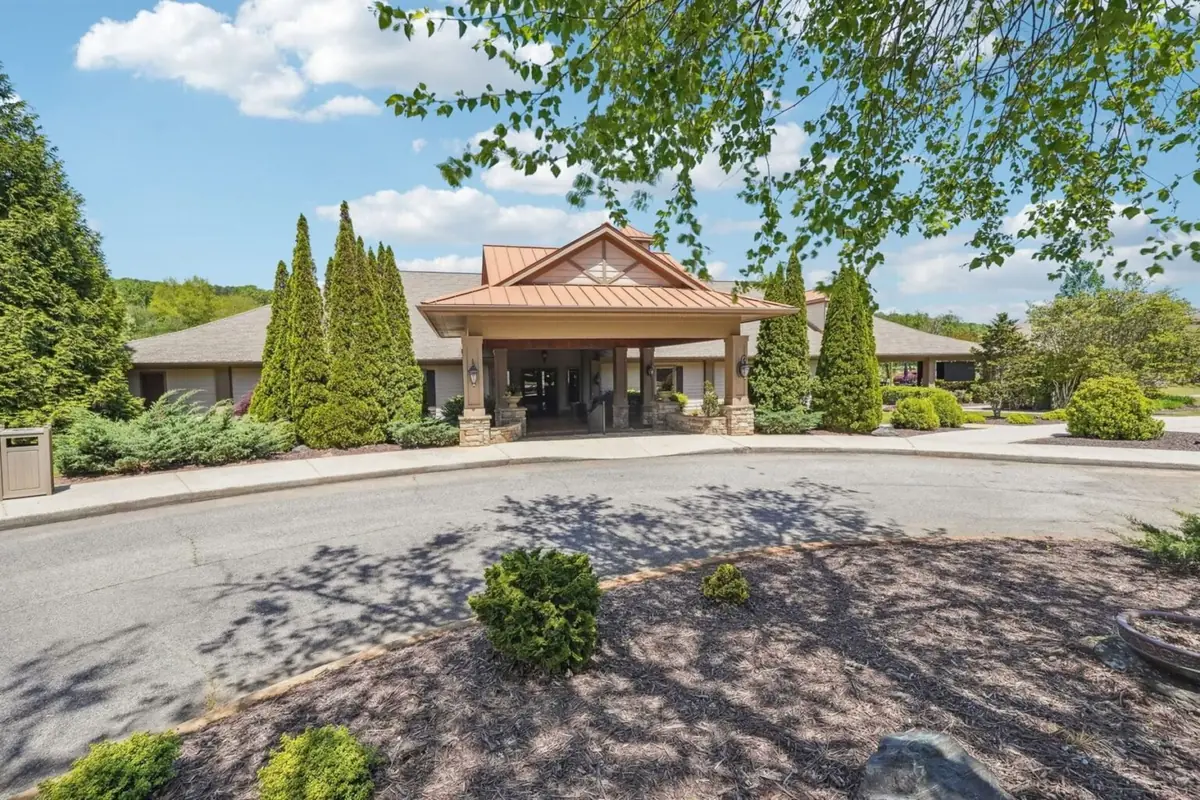 Front entrance of the Achasta clubhouse with copper-toned gable porte-coch&egrave;re, topiary, and a paved circular drive