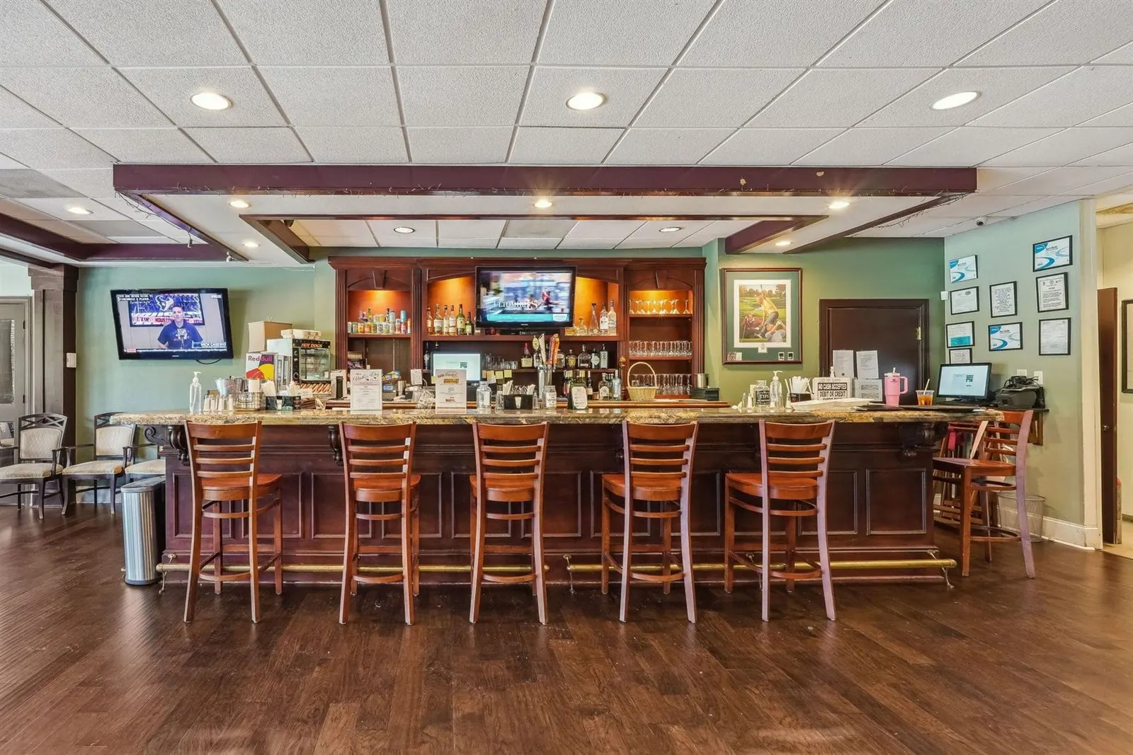 Achasta clubhouse bar — dark wood bar with six wooden stools, mounted TV screens, dark plank flooring