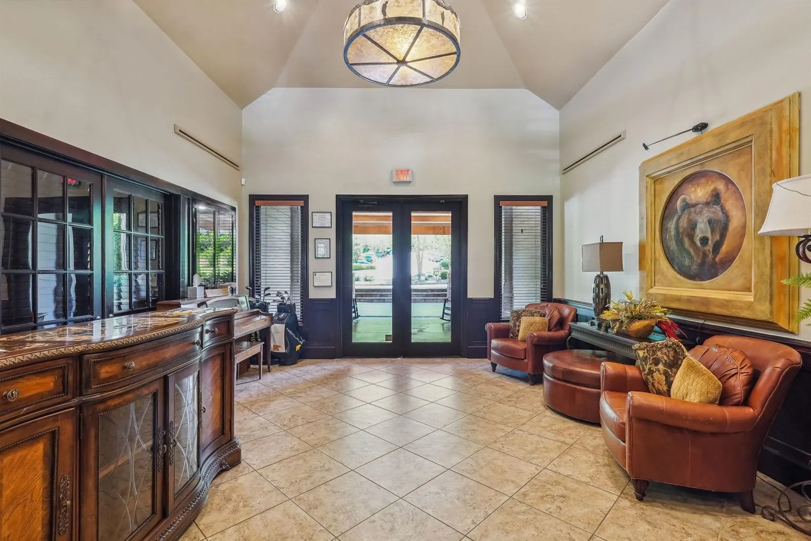 Achasta clubhouse foyer and pro shop entry — vaulted ceiling, antler-style chandelier, leather club chairs, and glass doors looking out to the porte-cochère