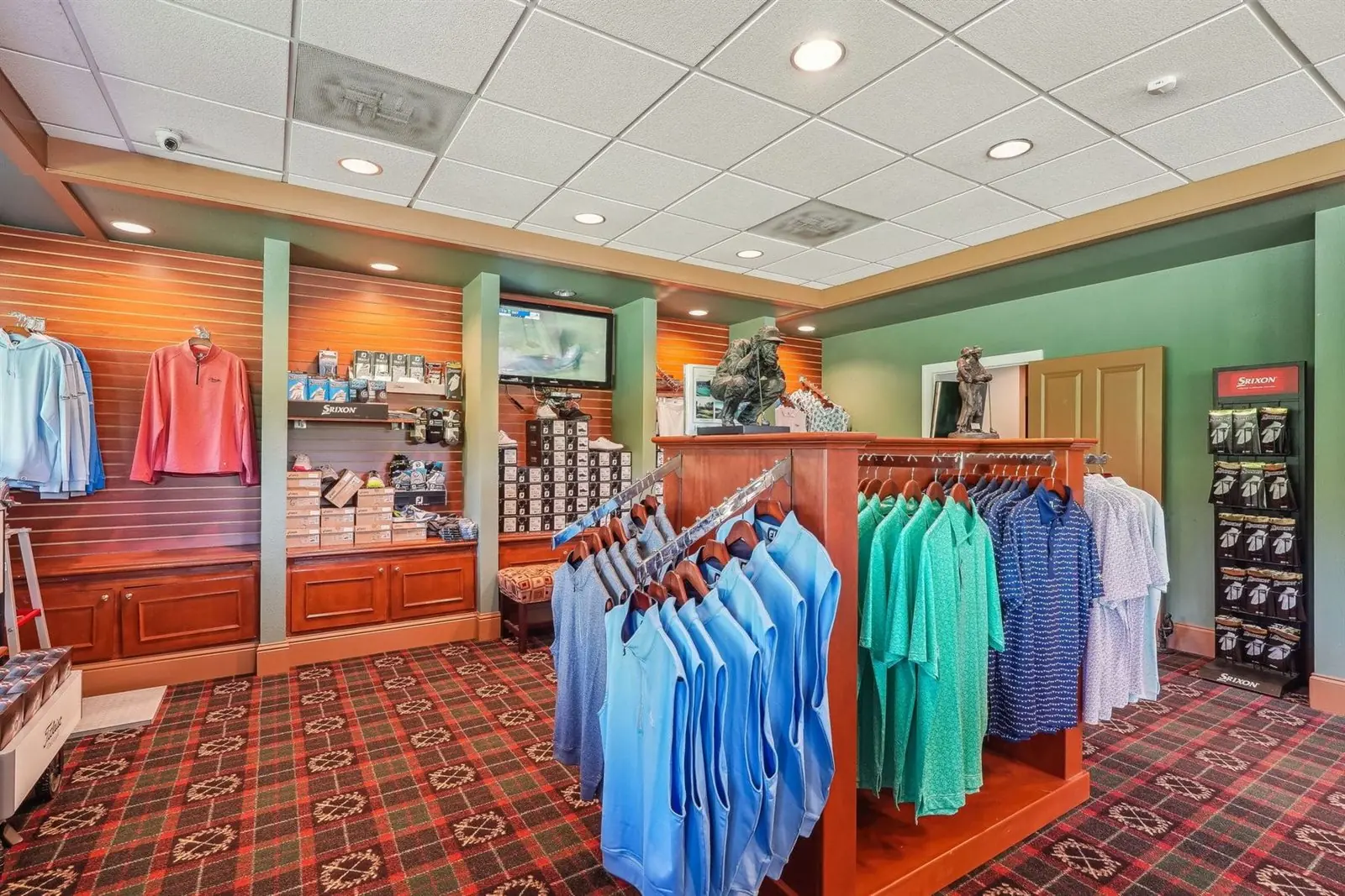 Interior of the Achasta pro shop with golf polo shirts on racks, plaid red and green carpet, and an apparel display island