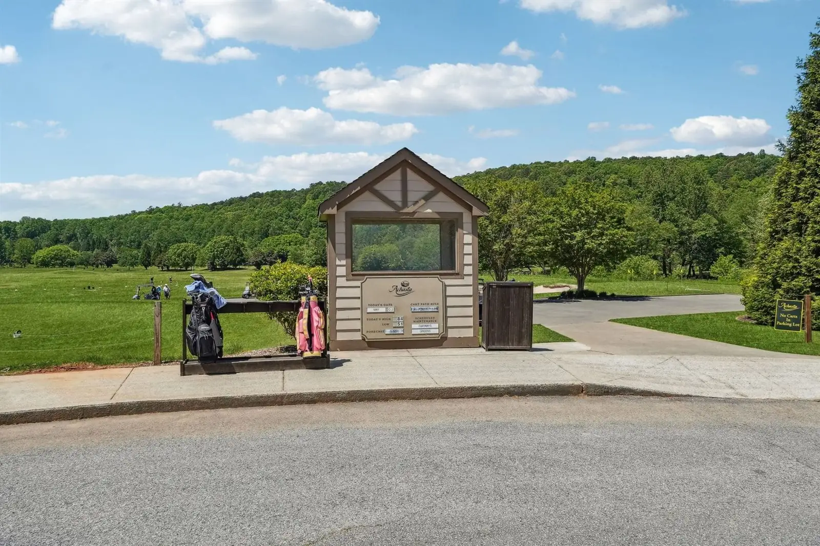 Cart staging kiosk at the edge of the Achasta practice area — a small wood and stone information stand with two golf bags parked beside it