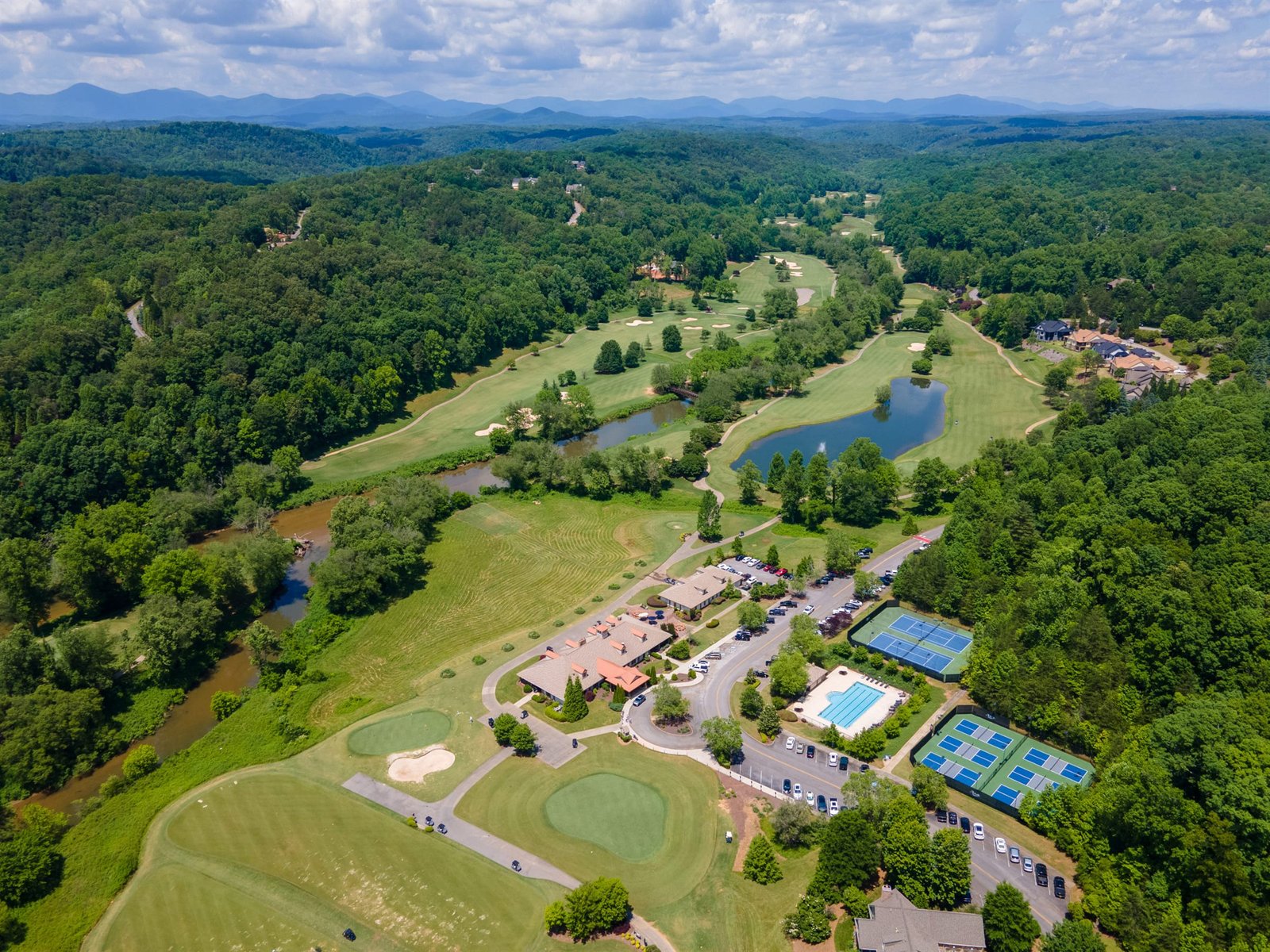 Wide aerial drone view of the Achasta community core in Dahlonega Georgia &mdash; clubhouse, tennis and pickleball courts, swimming pool, golf course, Chestatee River, and Blue Ridge foothills