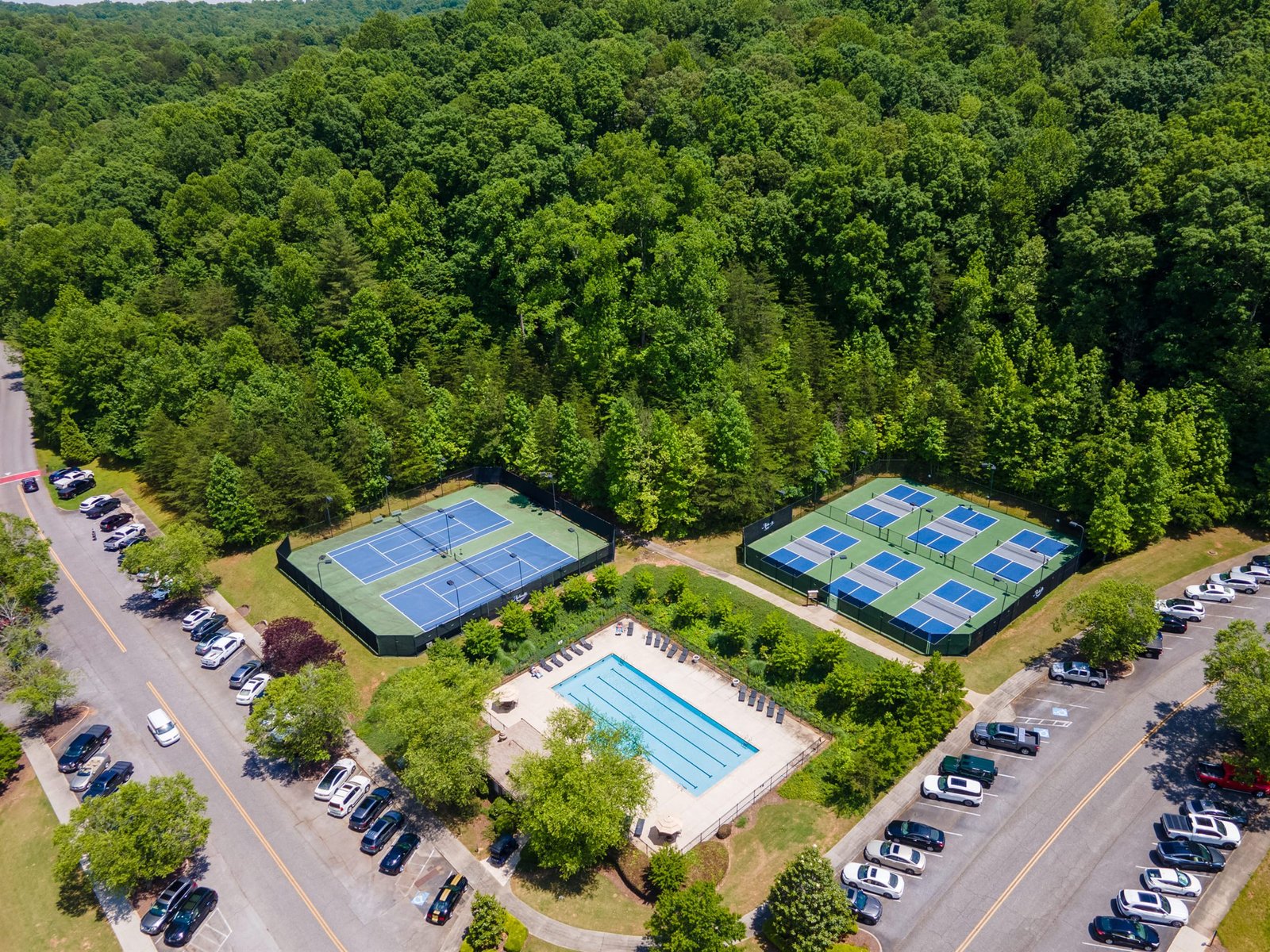 Top-down aerial view of the Achasta swimming pool with two hard tennis courts and six pickleball courts in two rows