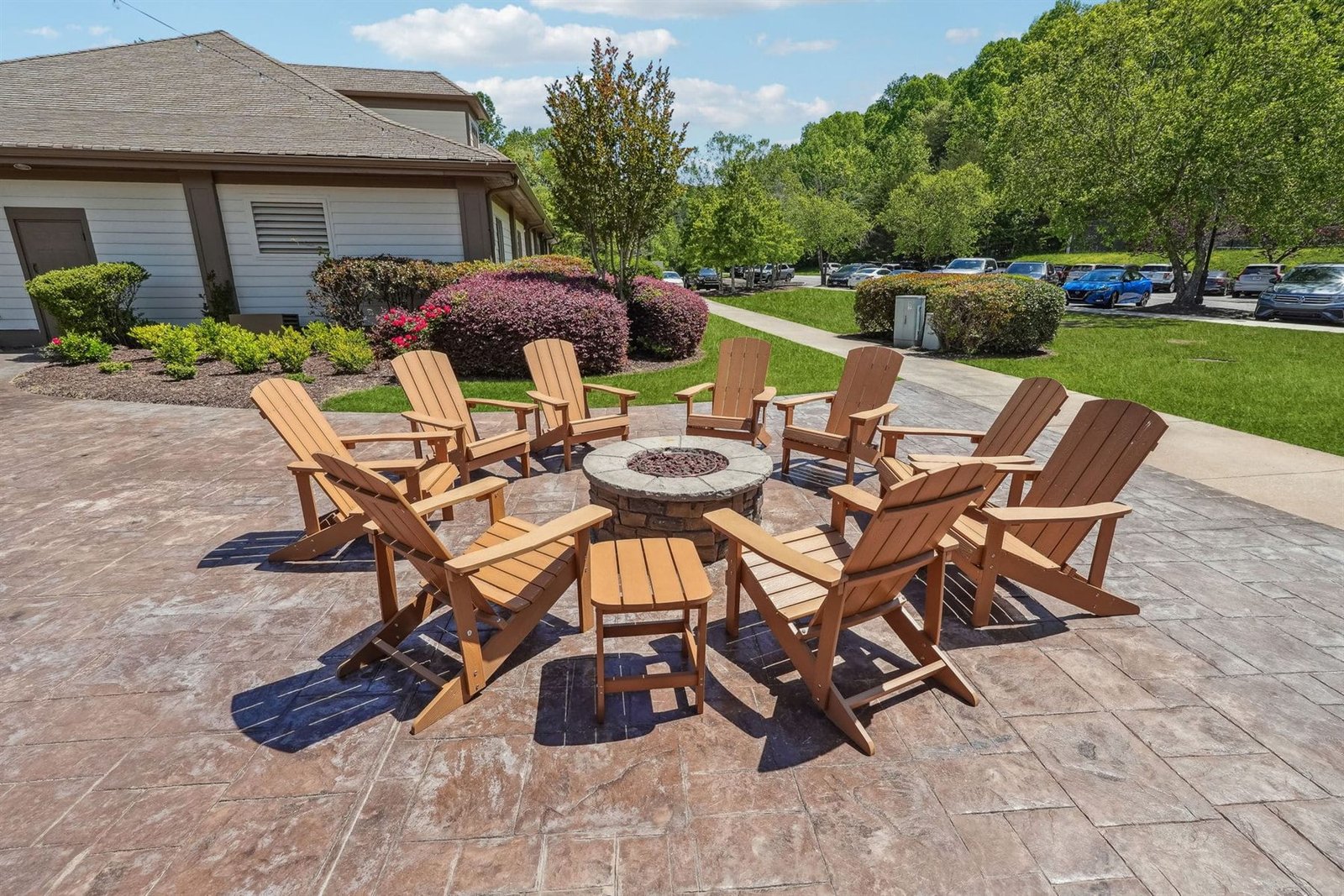 Outdoor firepit lounge at the Achasta clubhouse &mdash; eight cedar Adirondack chairs arranged around a stone gas firepit on a stamped concrete patio