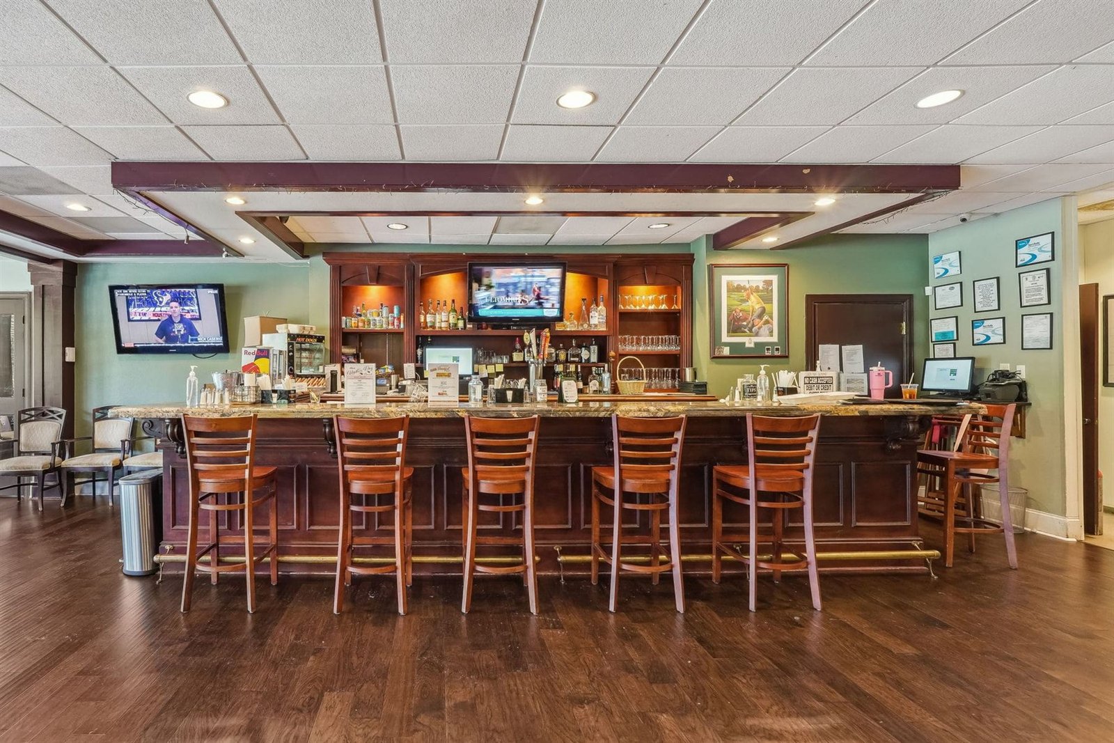 Achasta clubhouse bar &mdash; dark wood bar with six wooden stools, mounted TV screens, dark plank flooring