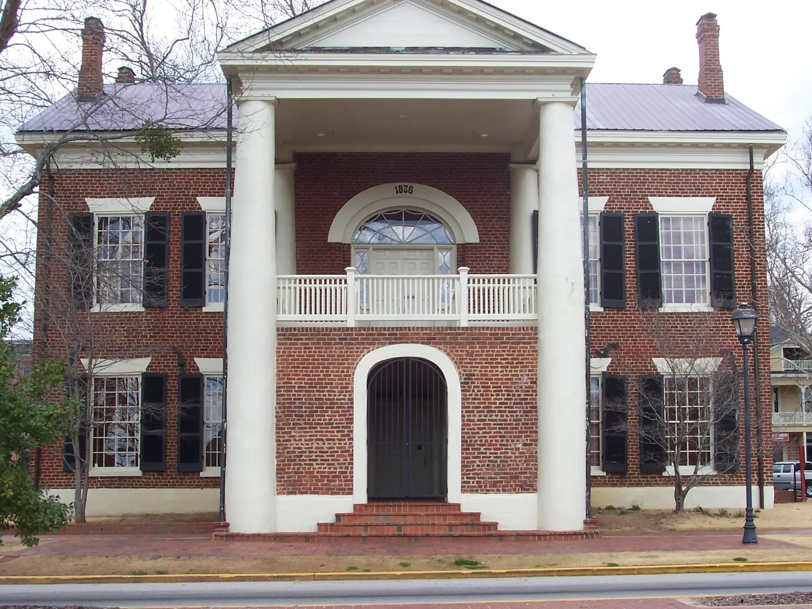 The historic 1836 Lumpkin County courthouse on the Dahlonega square, now the Dahlonega Gold Museum: red brick with a white-columned two-story portico, a balcony and an arched entry.